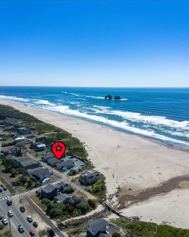 Aerial view of beachfront homes with sandy beach, ocean waves, and coastal road